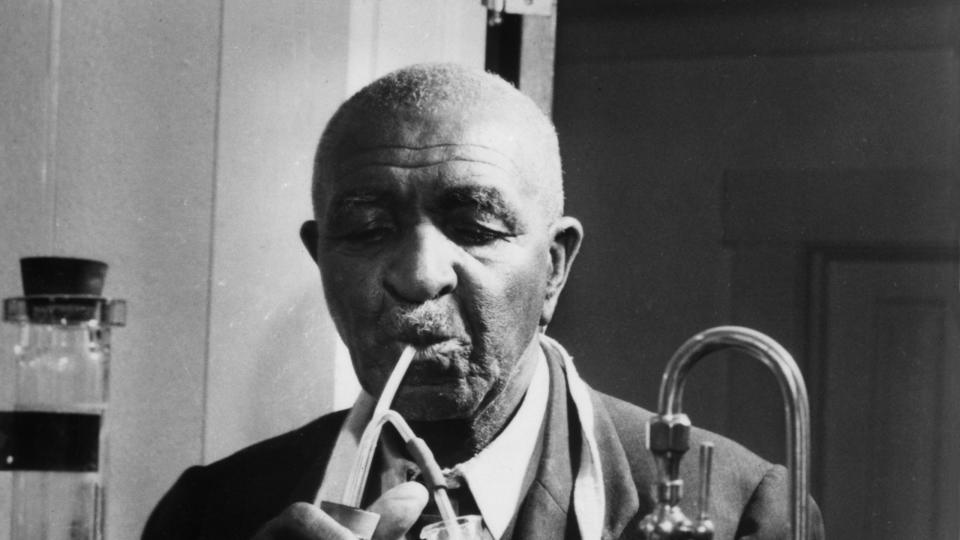 george washington carver holding a beaker and test tube while working on an experiment