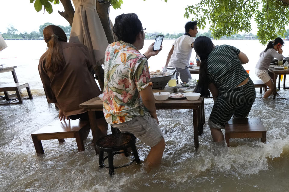 Customers of the riverside Chaopraya Antique Café react to a boat's wake as they enjoy themselves in the extraordinary high water levels in the Chao Phraya River in Nonthaburi, near Bangkok, Thailand, Thursday, Oct. 7, 2021. The flood-hit restaurant has become an unlikely dining hotspot after fun-loving foodies began flocking to its water-logged deck to eat amid the lapping tide. Now, instead of empty chairs and vacant tables the cafe is as full as ever, offering an experience the canny owner has re-branded as “hot-pot surfing.” (AP Photo/Sakchai Lalit)