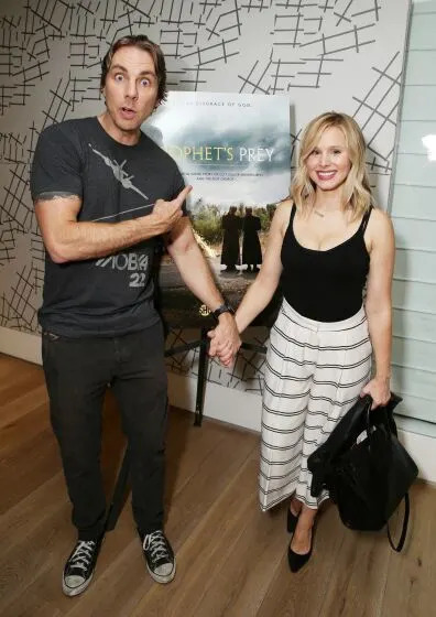 Dax Shepard and Kristen Bell posing in front of a film poster while holding hands.