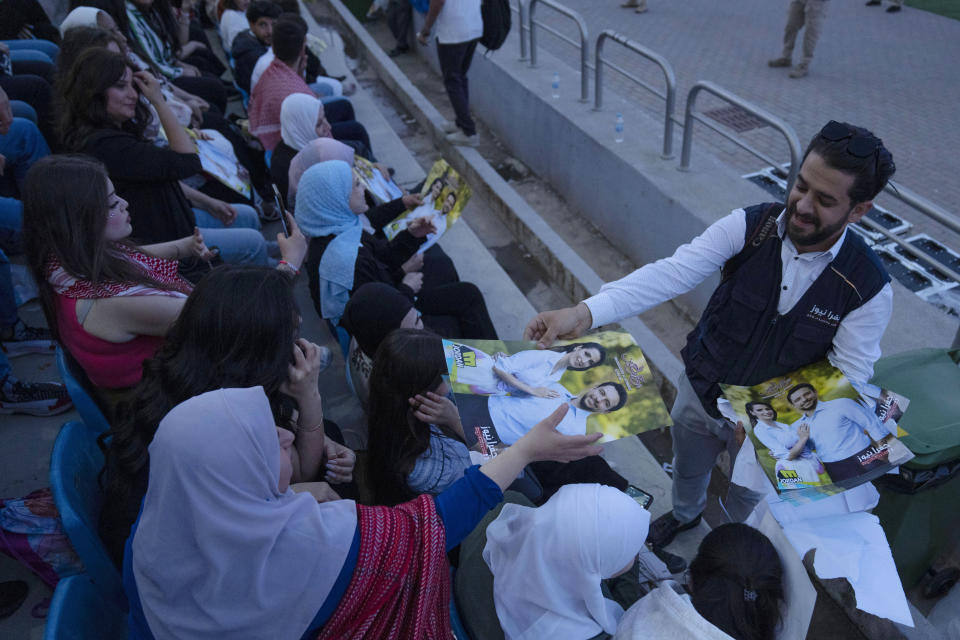 A man hands out posters of Jordan's Crown Prince Hussein and his fiancee, Saudi architect Rajwa Alseif, during a concert at a sports stadium in Amman, Jordan, Monday, May 29, 2023. The free concert featuring well-known Arab singers, including Egyptian star Tamer Hosny, was part the celebrations leading up to the couple's wedding later this week. (AP Photo/Nasser Nasser)