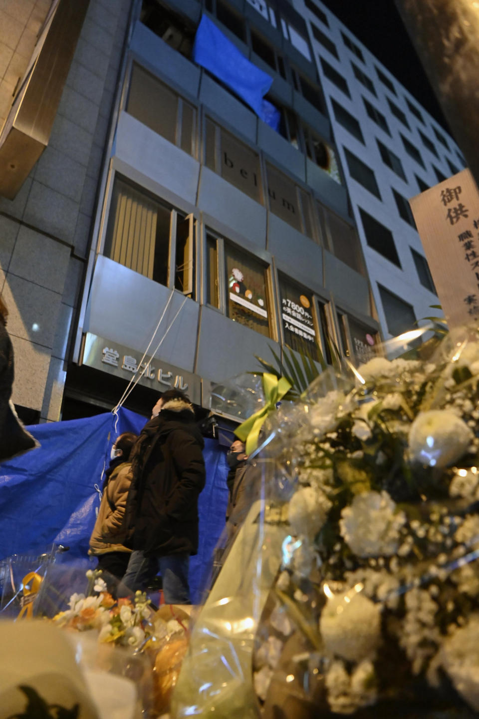 Offerings are placed near a building, background, where a fire broke out, in Osaka, western Japan Thursday, Dec. 30, 2021. The suspect in the fire that killed 25 people died Thursday at a hospital where he was being treated for burns and smoke inhalation, police said Friday. (Kyodo News via AP)