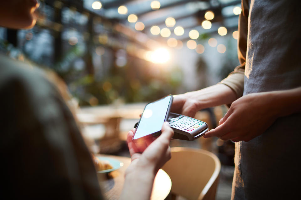 Close-up of unrecognizable woman using modern gadget while making online payment in cafe, nfc technology concept