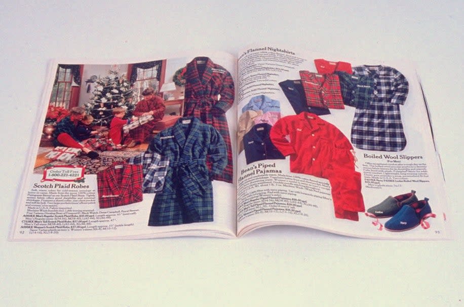 Open catalogue featuring Scotch plaid robes, pajamas, slippers, and various clothing items displayed on pages. The image includes holiday décor in the background