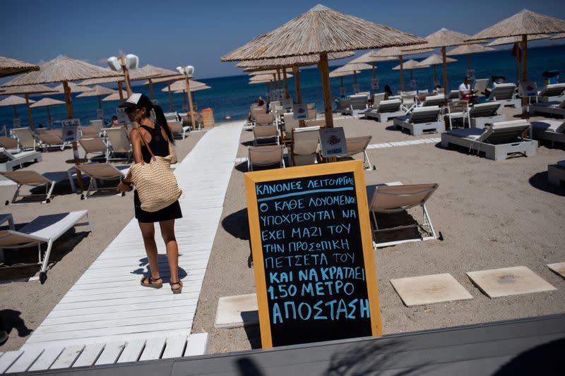 A woman walks past an announcement calling for customers to maintain social distancing at a beach bar, following the coronavirus disease (COVID-19) outbreak, on the island of Kos