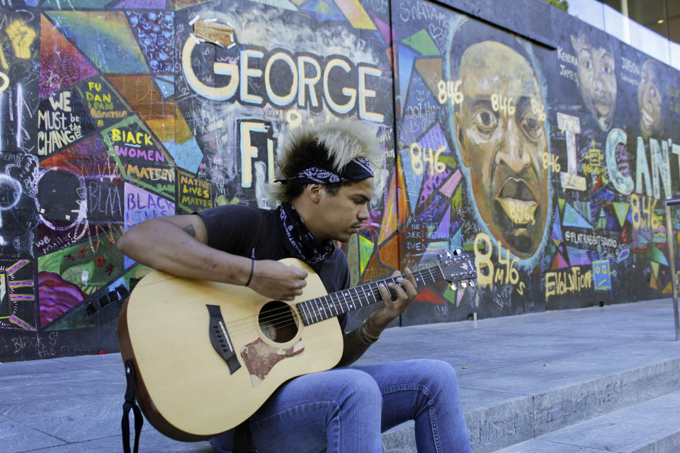 FILE - In this Aug. 27, 2020, file photo, Shane Braswell, who has protested at least 60 days since late May, spends an afternoon playing acoustic guitar in front of a huge mural in downtown Portland, Ore., that's dedicated to Black people killed by police. Once hailed as one of the most livable cities in the U.S., Portland is grappling with an uncertain future as it reaches a stunning benchmark: 100 consecutive nights of racial injustice protests marred by vandalism, chaos — and now, the killing of a supporter of President Donald Trump. (AP Photo/Gillian Flaccus, File)