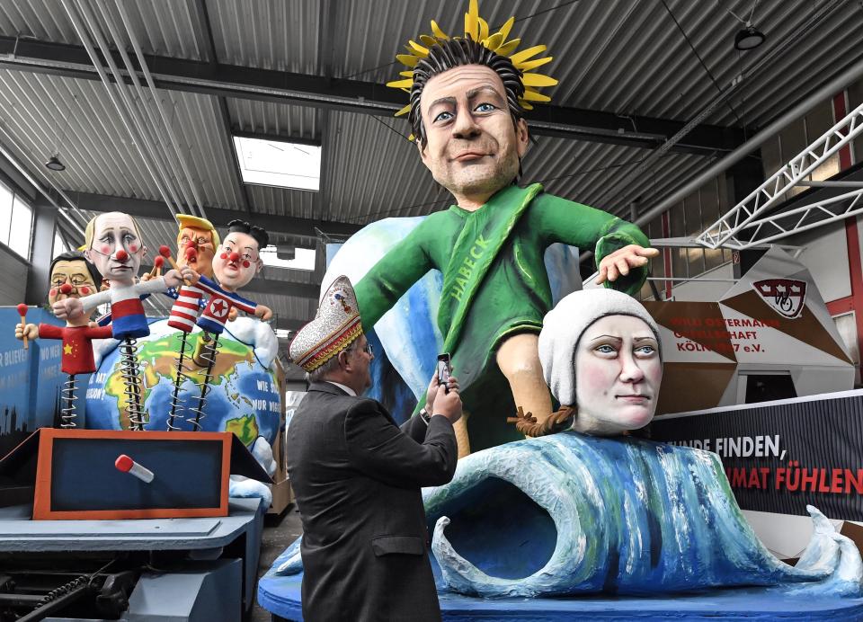 A satiric carnival float depicting climate activist Greta Thunberg and German Green leader Robert Habeck surfing on her wave, is pictured by a reveller during a preview in a hall in Cologne, Germany, Tuesday, Feb. 18, 2020. The traditional carnival parades on Rosemonday make fun of politics and are watched by hundreds of thousands in the streets of Cologne, Duesseldorf and Mainz. (AP Photo/Martin Meissner)