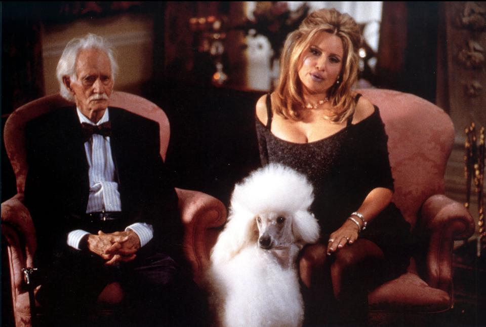 Jim Cranshaw and Jennifer Coolidge sitting on fancy chairs with a fluffy standard poodle at their feet