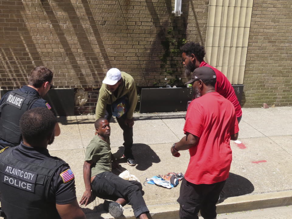 City outreach workers and police officers try to help a man sprawled on a sidewalk in Atlantic City, N.J., on Monday, July 1, 2024, the date city officials announced implementation of programs to address homelessness. (AP Photo/Wayne Parry)