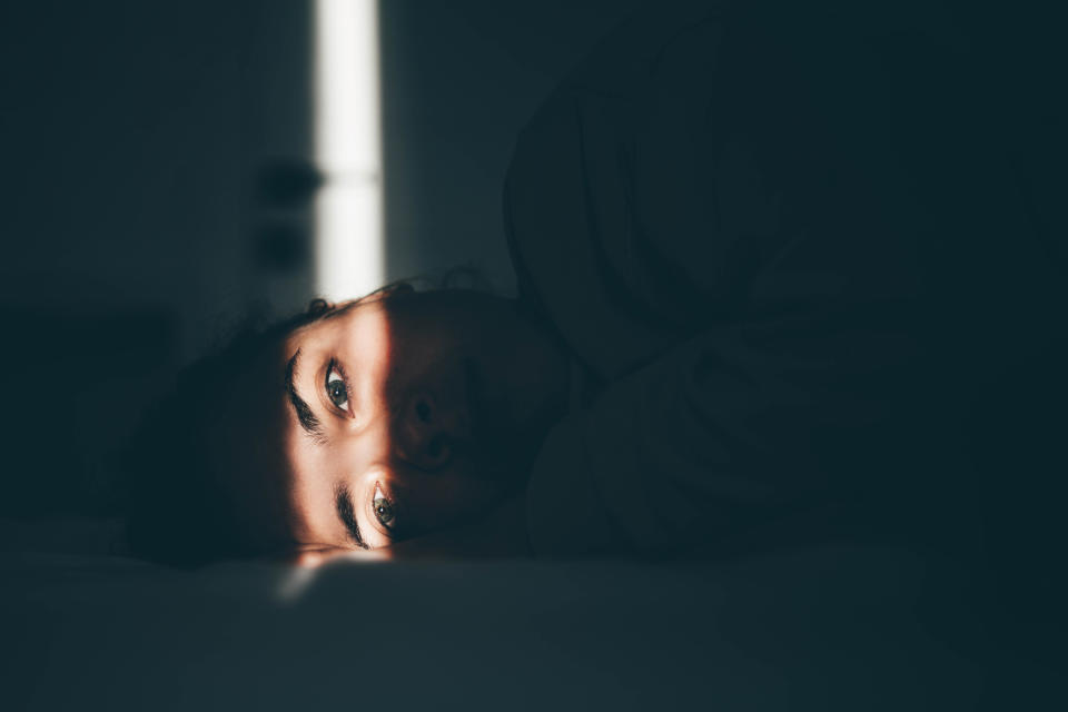 A person lays on a bed with a faint beam of light illuminating their eyes and part of their face. The surroundings are dimly lit, creating a calm atmosphere