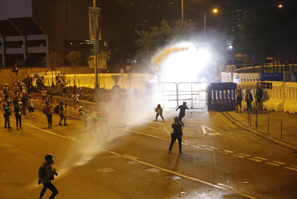 Police fire water canon on protestors in Hong Kong, Saturday, Sept. 28, 2019. Protesters streamed onto a main road nearby and some targeted government buildings that were barricaded. Police initially used a hose to fire pepper spray after some demonstrators threw bricks. A water cannon truck later fired a blue liquid, used to identify protesters, after protesters lobbed gasoline bombs through the barriers. (AP Photo/Vincent Thian)