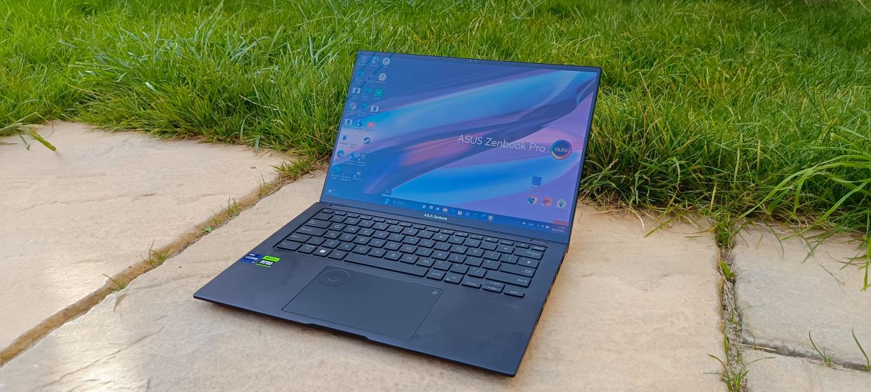  A black ASUS Zenbook Pro 14 OLED sitting on a patio in front of a grassy lawn. 