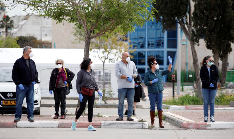 Israelis wearing masks and gloves stand next to a special polling station set up by Israel's election committee so Israelis under home-quarantine can vote, in Ashkelon