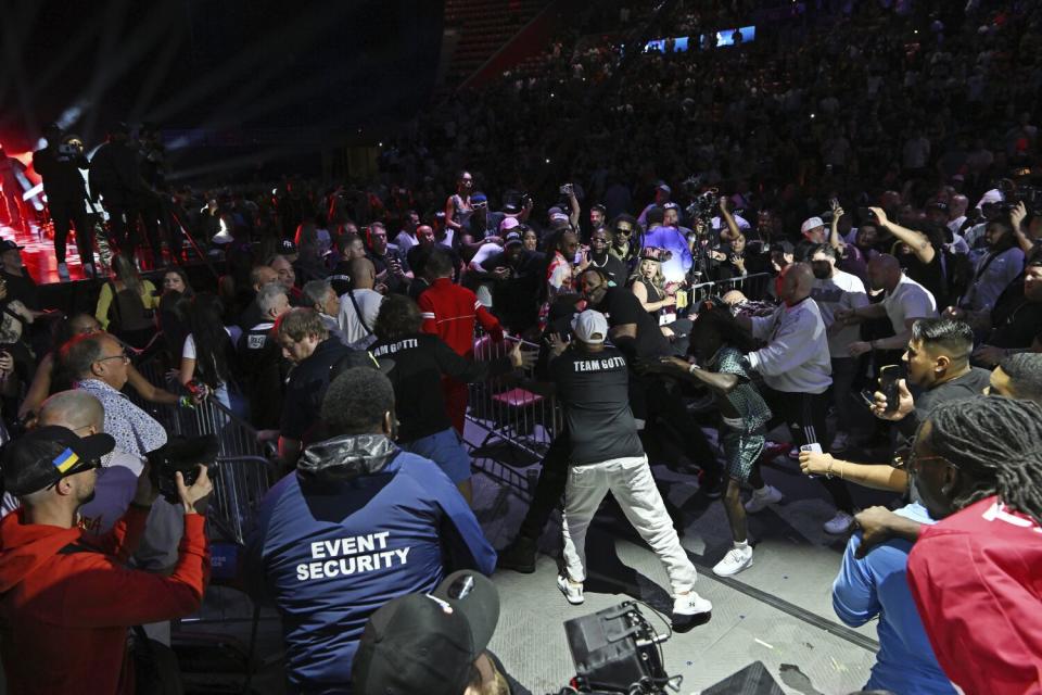 A large gaggle of people surrounds an area off of a boxing ring.