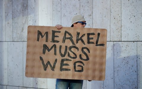 A protestor holds a placard reading "Merkel must go" outside the CDU headquarters - a sight that may become more common - Credit:  AXEL SCHMIDT/ REUTERS