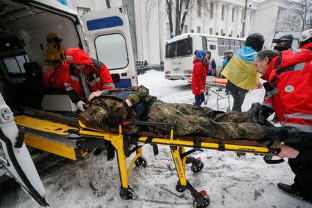 A wounded protester is rushed to an ambulance as riot police look on, near the parliament building in Kiev, Ukraine March 3, 2018. REUTERS/Gleb Garanich