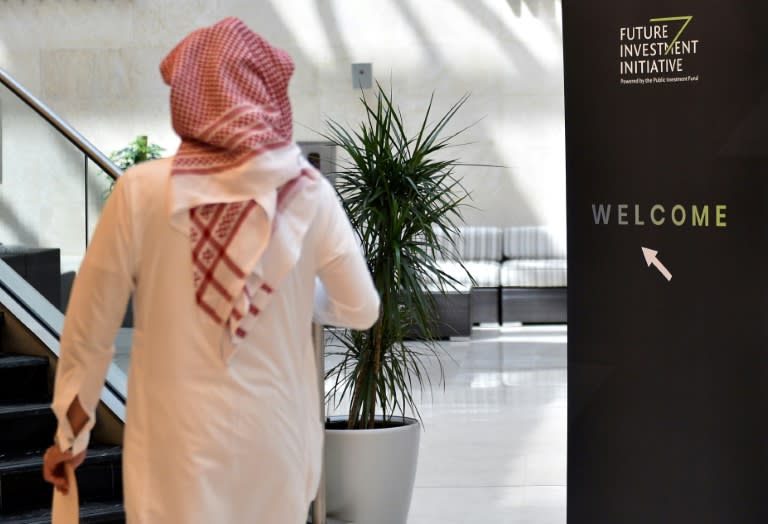 A picture taken on October 22, 2018 shows a Saudi man walking next to a sign of the Future Investment Initiative FII one day ahead of the three-day conference in Riyadh