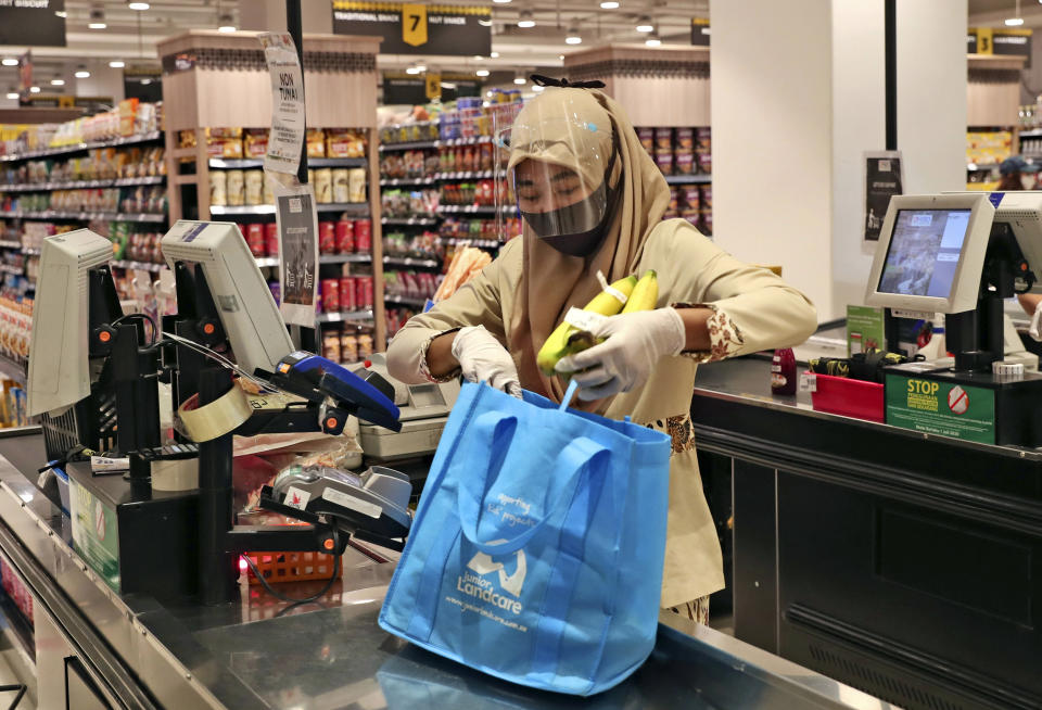 A staff wearing protective gear as a precaution against the new coronavirus outbreak checks out a customer at a supermarket in Jakarta, Indonesia, Wednesday, July 1, 2020. The government of Indonesia's capital region is extending the first transition phase from large-scale social restrictions in Jakarta as the number of new confirmed coronavirus cases continues to rise. (AP Photo/Tatan Syuflana)