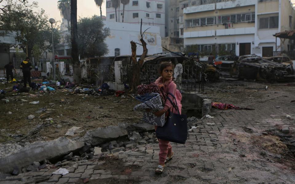 A Palestinian girl carries a blankets as she walks past the explosion site at Ahli Arab Hospital in Gaza City