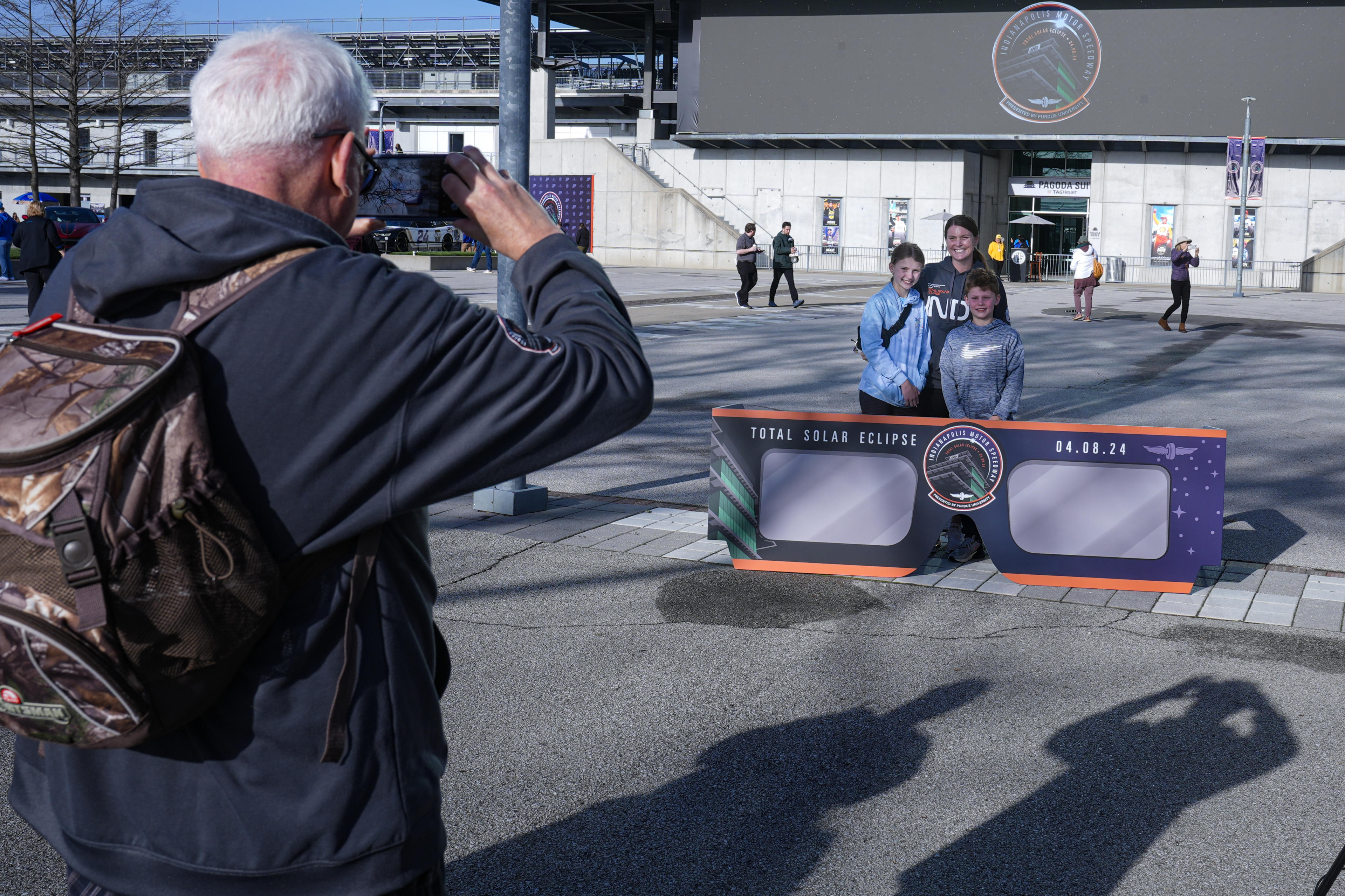 A family poses for a photo with a large eclipse glasses display in front of the pagoda at the Indianapolis Motor Speedway in Indianapolis.A family poses for a photo with a large eclipse glasses display in front of the pagoda at the Indianapolis Motor Speedway in Indianapolis, Monday, April 8, 2024. (Michael Conroy/AP)