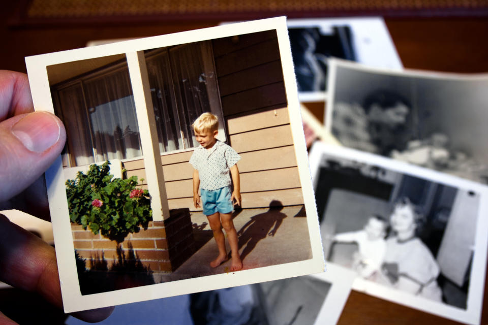 Hand holding a photograph of a child standing in front of a door, with more photos beneath