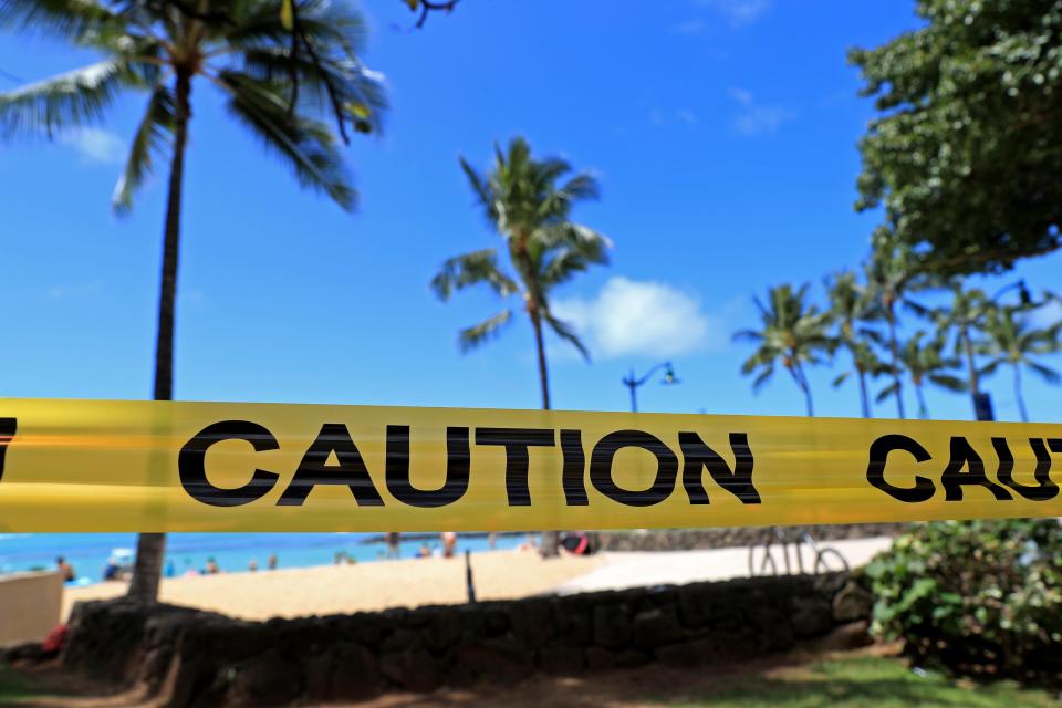 With beachgoers in the background, yellow caution tape is wrapped across an area of Waikiki, Friday, March 20, 2020, in Honolulu.