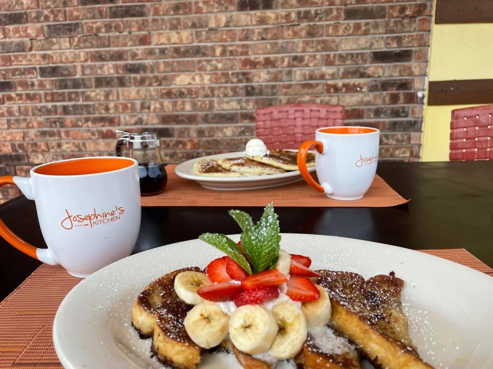 a plate of french toast with bananas and strawberries and mugs of coffee