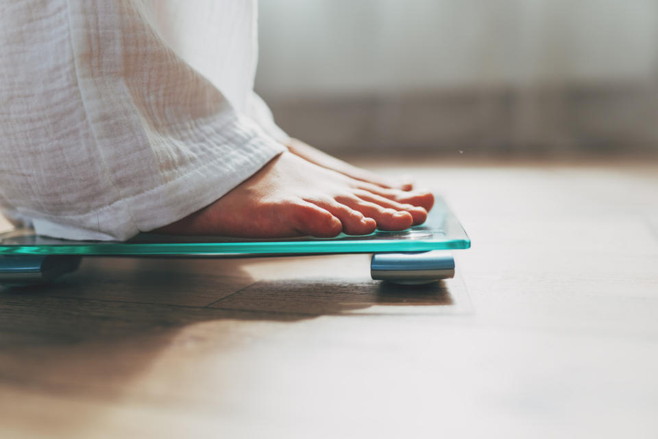 Close up of the feet of a person standing on a digital bathroom scale placed on a wooden floor