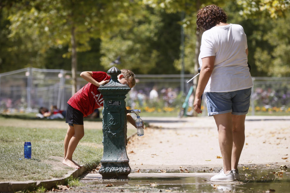 A child fills up a bottle at a water fountain in the Champ de Mars park, near the Eiffel Tower, Wednesday, July 13, 2022 in Paris. Temperatures in Paris are expected to rise up to 35 degrees Celsius (95 degrees Fahrenheit). (AP Photo/Thomas Padilla)