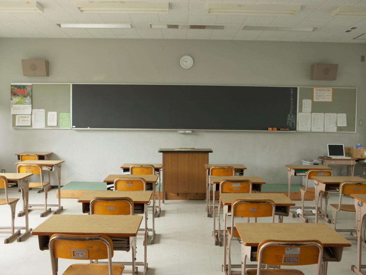 View of desks from the back of an empty classroom facing a chalkboard