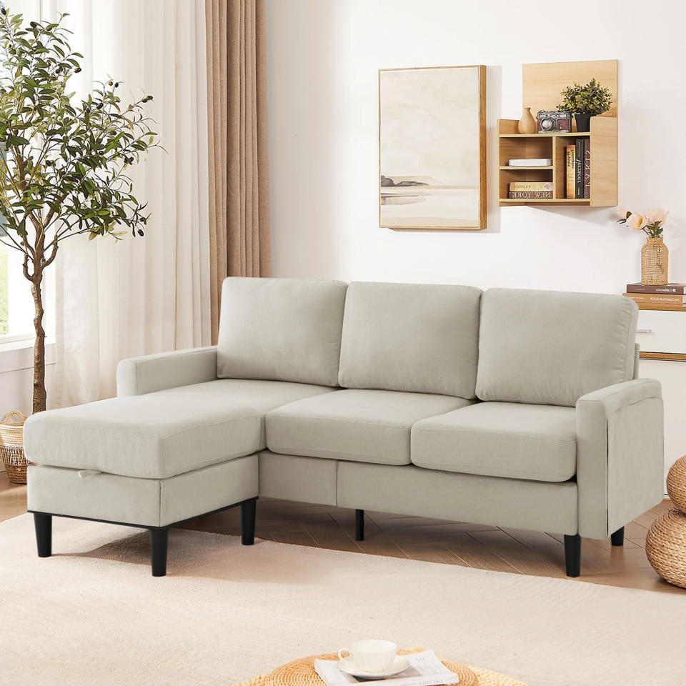 beige sectional sofa with black legs in a bright living room, featuring a wall painting, shelves, potted plant, and a round woven rug