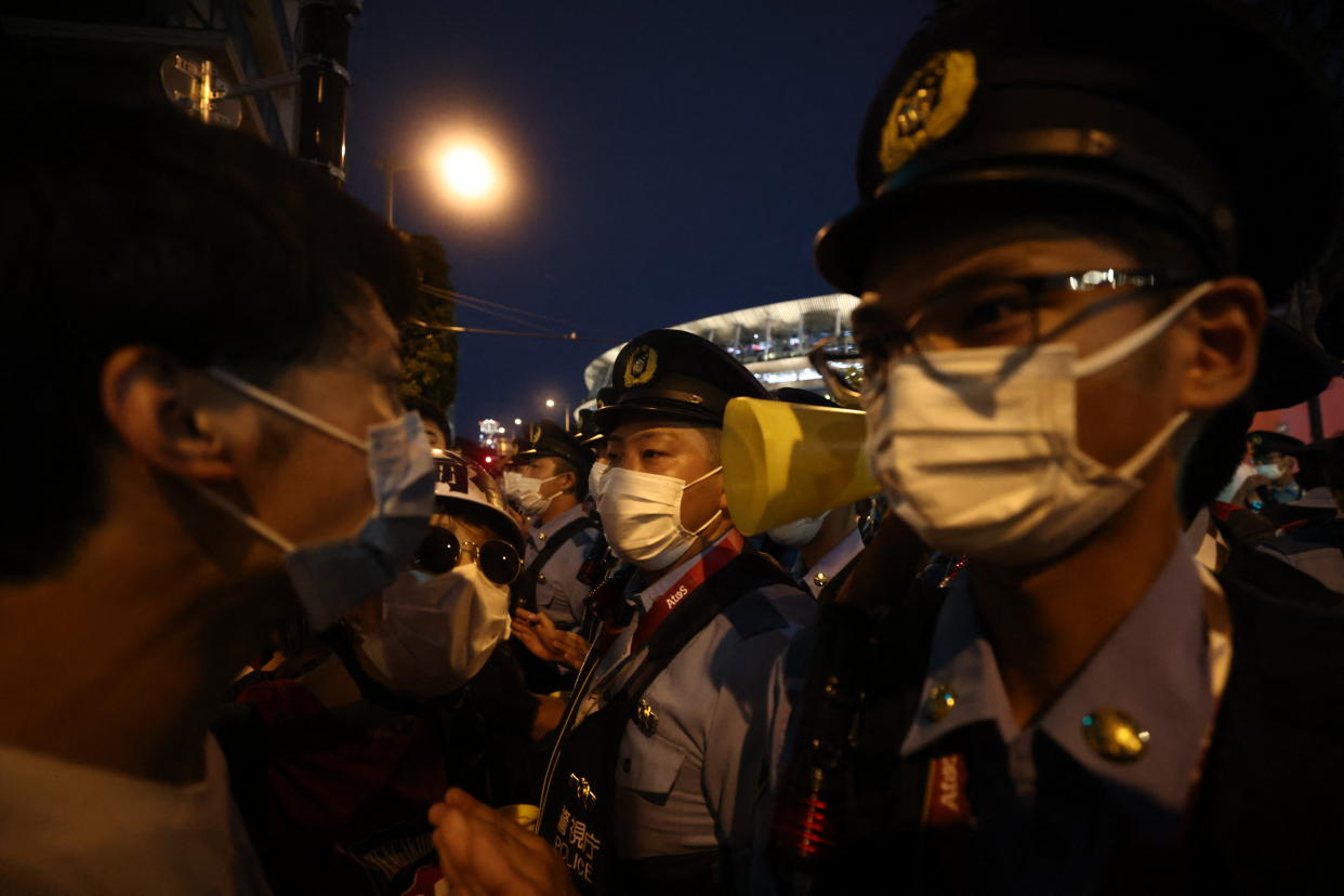 Police officers stand in front of protestors protesting against the Tokyo 2020 Olympic Games outside the Olympic Stadium ahead of the opening ceremony of the Tokyo 2020 Olympic Games, in Tokyo, on July 23, 2021. (Photo by Behrouz MEHRI / AFP) (Photo by BEHROUZ MEHRI/AFP via Getty Images)