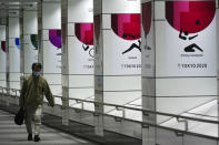 A man wearing a protective mask to help curb the spread of the coronavirus walks near banners of the Tokyo 2020 Olympics and Paralympics in Tokyo Tuesday, Jan. 19, 2021. The Tokyo Olympics are to open in six months on July 23. Interestingly, Tokyo organizers have no public program planned to mark the milestone. There is too much uncertainty for that right now. (AP Photo/Eugene Hoshiko)