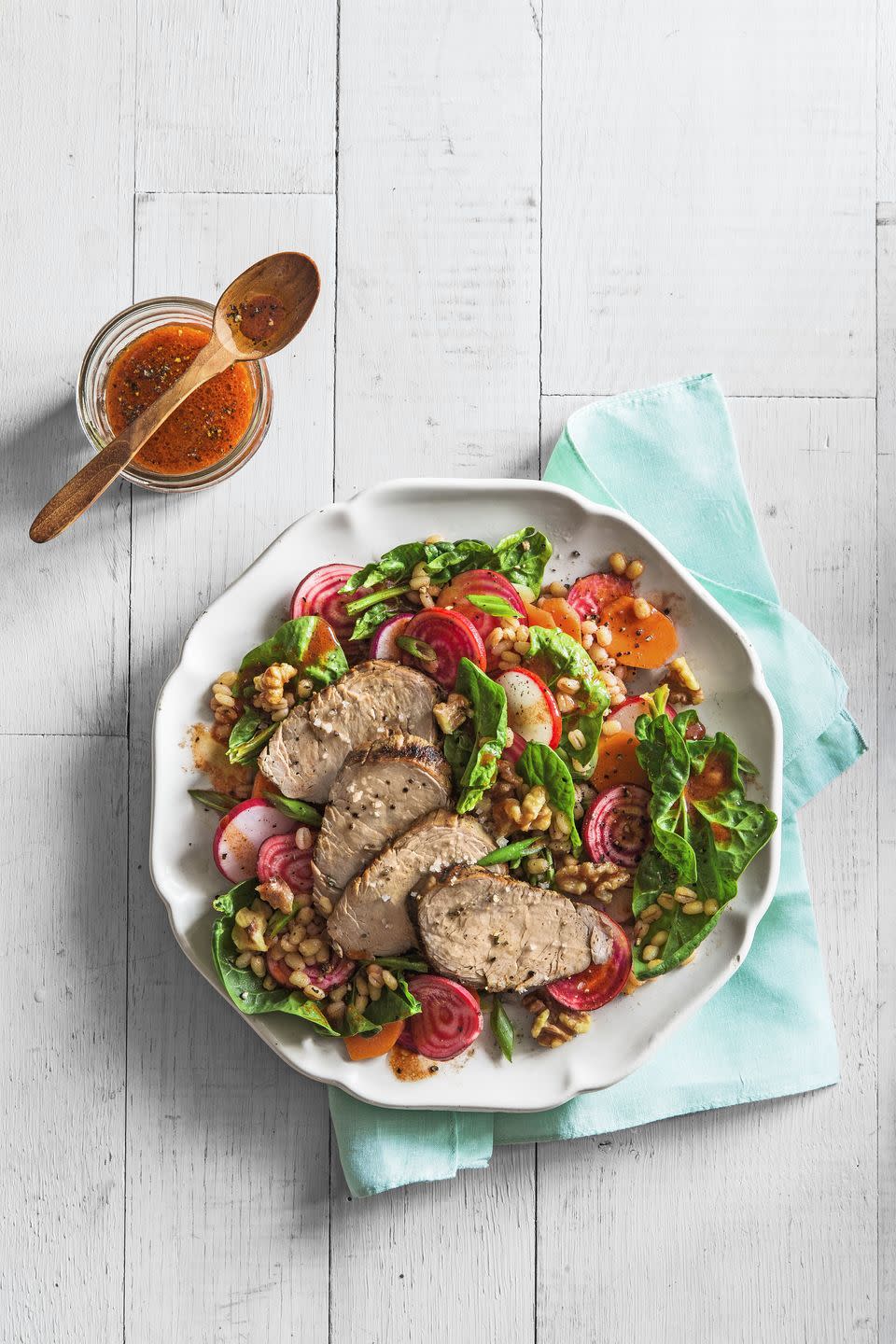 spinach and barley salad with grilled pork on a large white plate
