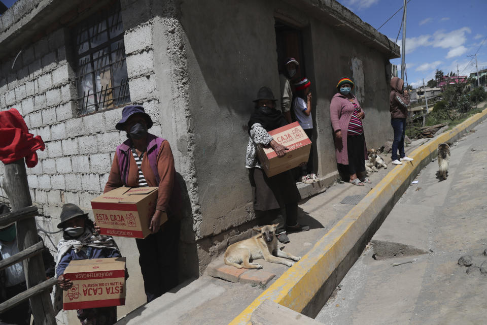 FILE - In this May 27, 2020, file photo, residents wearing protective face masks hold food boxes distributed by the government during a lockdown to contain the spread of COVID-19, on the outskirts of Quito, Ecuador. The coronavirus pandemic has brought hard times for many farmers and has imperiled food security for many millions both in the cities and the countryside. (AP Photo/Dolores Ochoa, File)