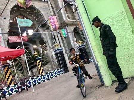 A boy rides a bicycle while looking at an army soldier stationed in front of a Sufi mosque in Kattankudy