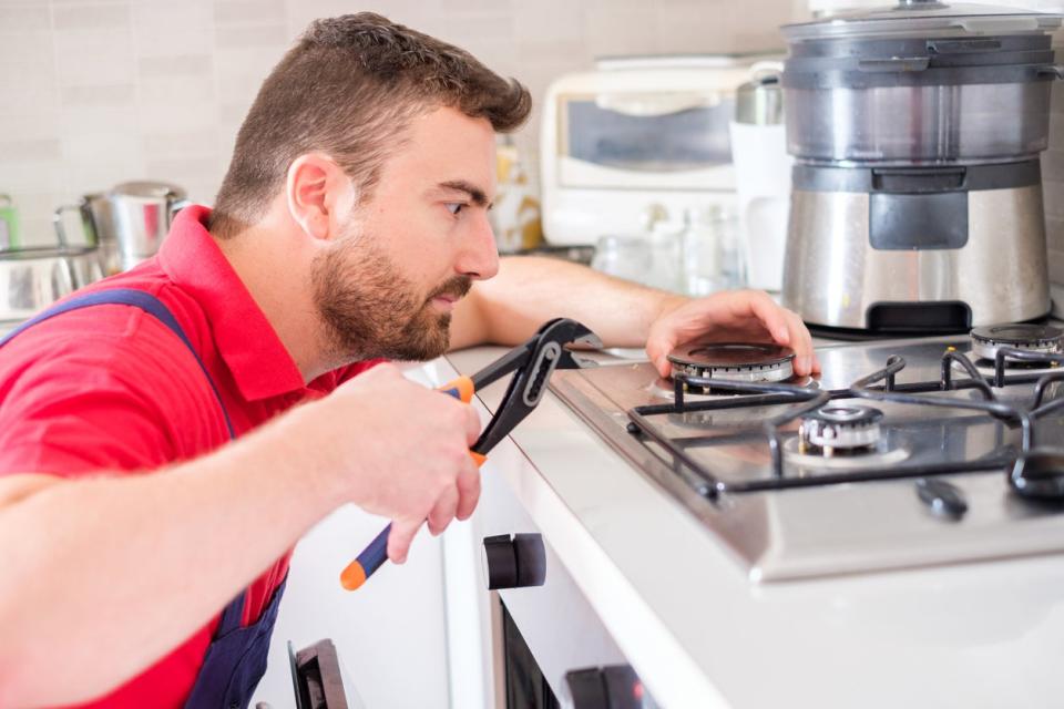 Handyman fixing gas stove in the kitchen.