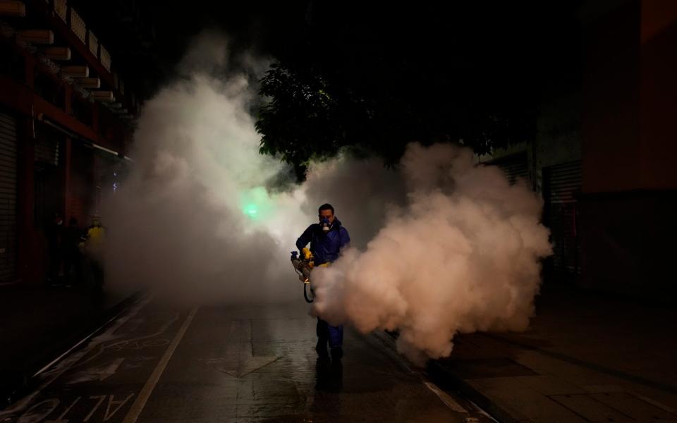 A worker in personal protective equipment sanitizes a street in the wake of a spike in the number of positive coronavirus cases, in downtown Guatemala City - Moises Castillo/AP