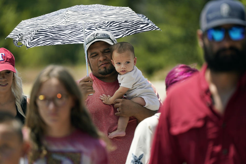 Kelci Gonzales uses an umbrella to shield his his six-month-old son Micaa Gonzales from the sun as they make their way to a sporting event in Arlington, Texas, Saturday, Aug. 19, 2023. (AP Photo/LM Otero)