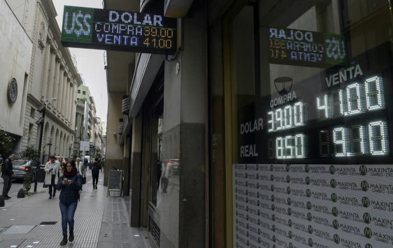 Pedestrians walk by a Buenos Aires exchange bureau where the buy-sell board displays the Argentine peso exchange values