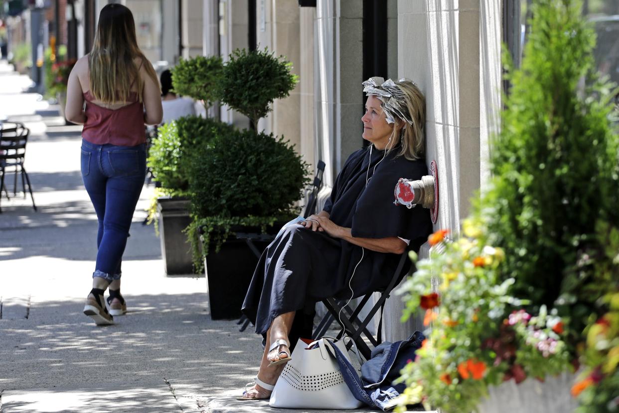 A woman sits as she waits to get her hair done outside of a hair salon in Winnetka, Ill. on Tuesday, June 23, 2020. Gatherings of up to 50 people will be allowed across the state starting Friday as Illinois moves into the fourth phase of its reopening plan. Phase four includes businesses such as hair salons, hair braiders, barber shops, nail salons, spas, massage therapy clinics, waxing centers, tattoo parlors and tanning salons.