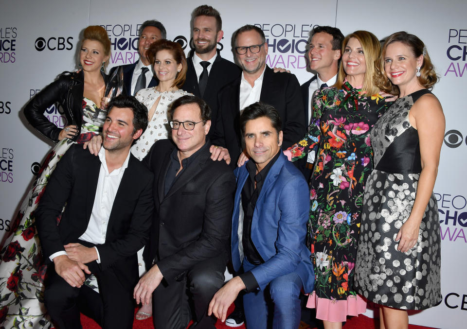 The "Full House" cast at the People's Choice Awards, posing for a photo on the red carpet. They are all dressed in elegant and stylish outfits