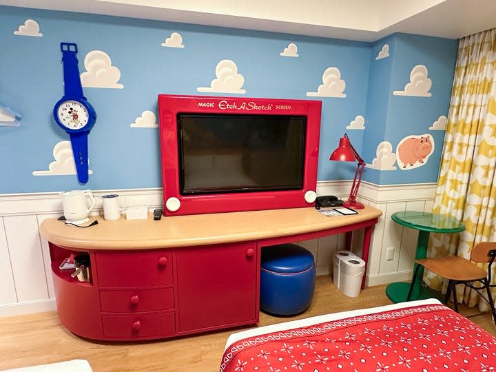 A view of the inside of a room at Tokyo's Toy Story Hotel stays on theme with a TV designed to look like an Etch-A-Sketch, a blue retro Mickey watch clock hanging on the wall and a red desk lamp that looks like Pixar's Luxo Jr.