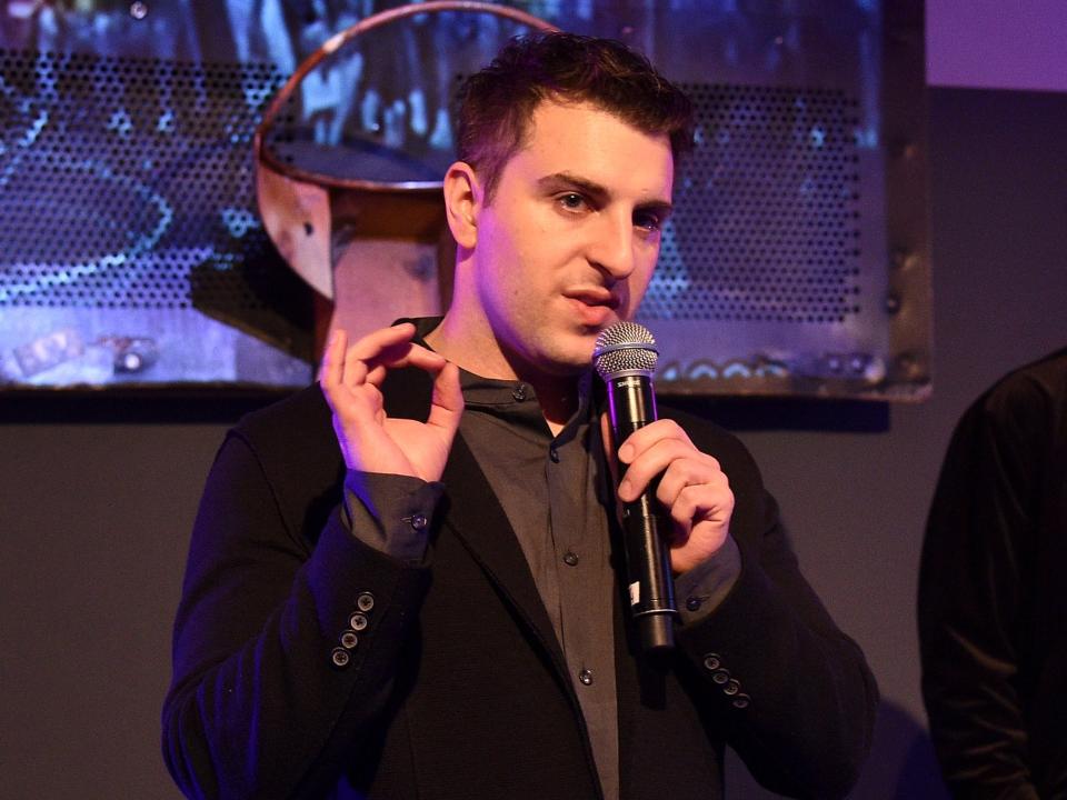 Brian Chesky holding a microphone and gesturing with his right hand