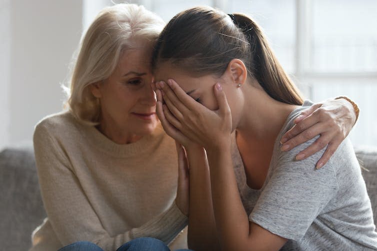 An older woman comforting her adult daughter, who has her face in her hands.