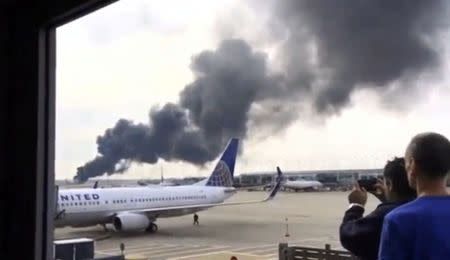 Smoke rises after an American Airlines jet (background) blew a tire, sparking a fire and prompting the pilot to abort takeoff before passengers were evacuated from the plane via emergency chute, at O'Hare International Airport in Chicago, Illinois, U.S., in this still image taken from video October 28, 2016. Courtesy of Robocast.com/Handout via REUTERS.