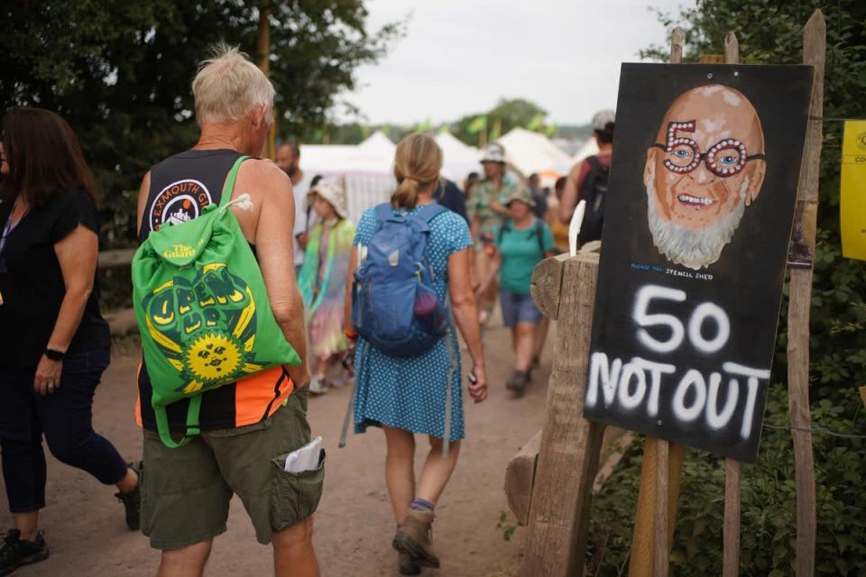Festival-goers walk past a Michael Eavis sign (Yui Mok/PA) (PA Wire)