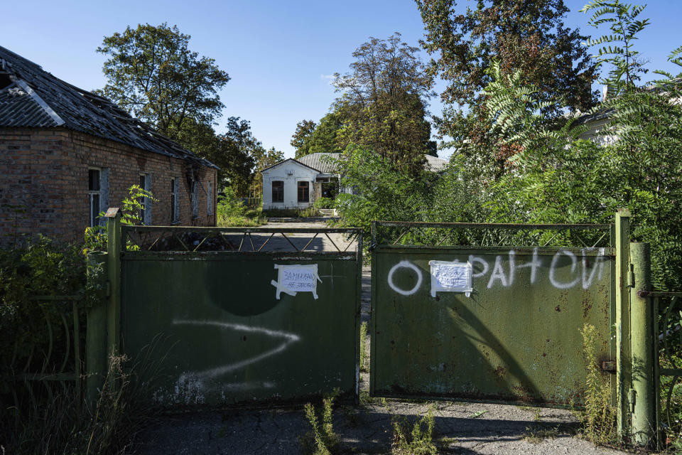 A gate stands in front of a former health clinic, background center, that had been used by Russian soldiers in Izium, Ukraine, Wednesday, Sept. 21, 2022. Ukrainian civilians said they were detained and tortured at the site. (AP Photo/Evgeniy Maloletka)