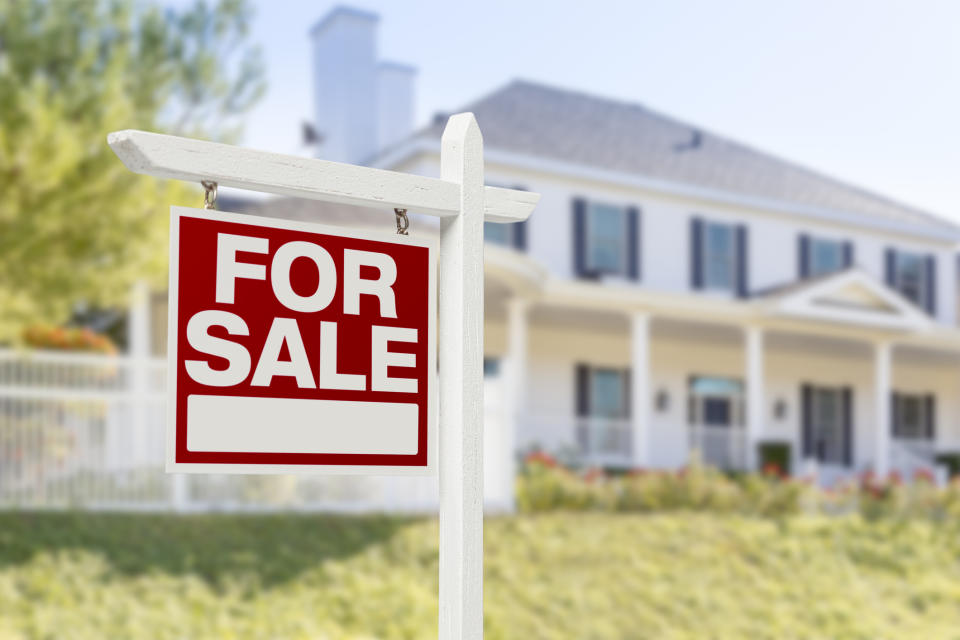 For Sale sign with out-of-focus house in the background