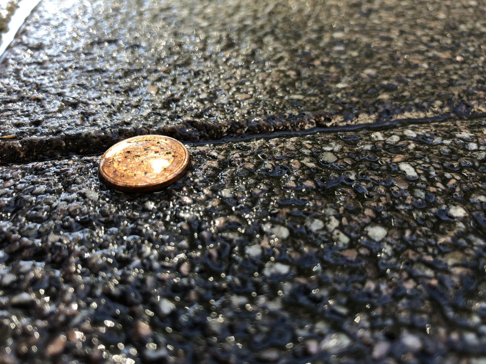 A single penny is lodged between two concrete slabs in an outdoor, textured pavement