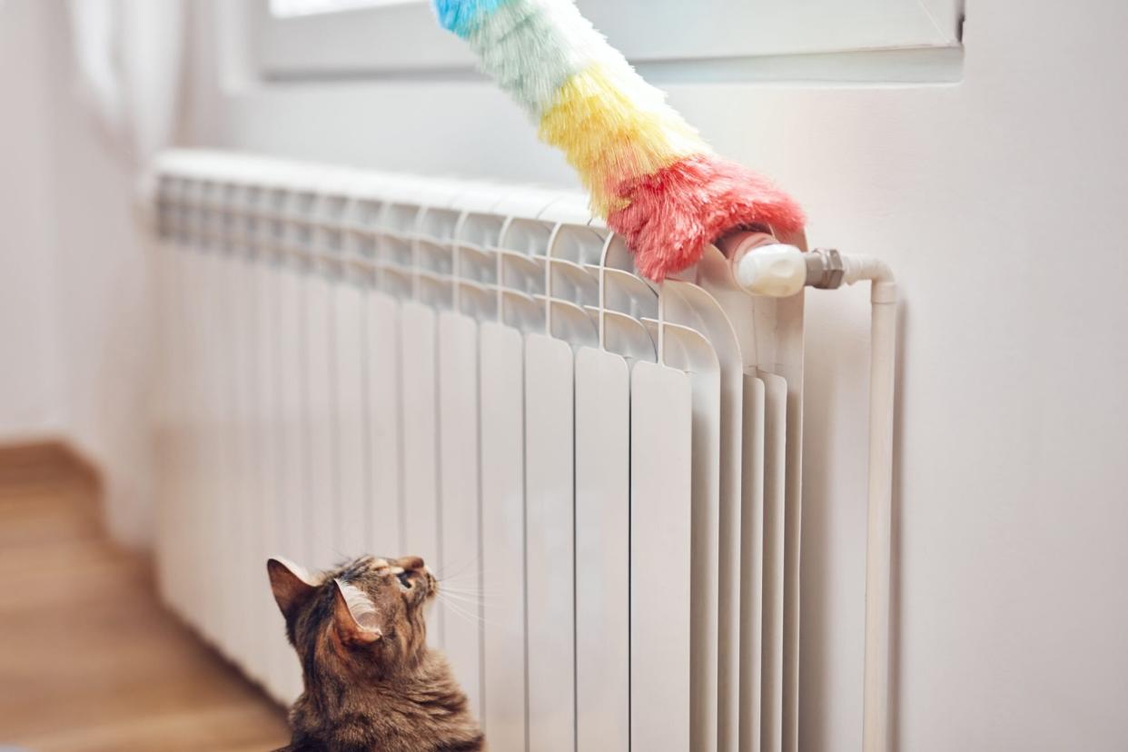 Woman with a dust stick cleaning central heating gas radiator at home